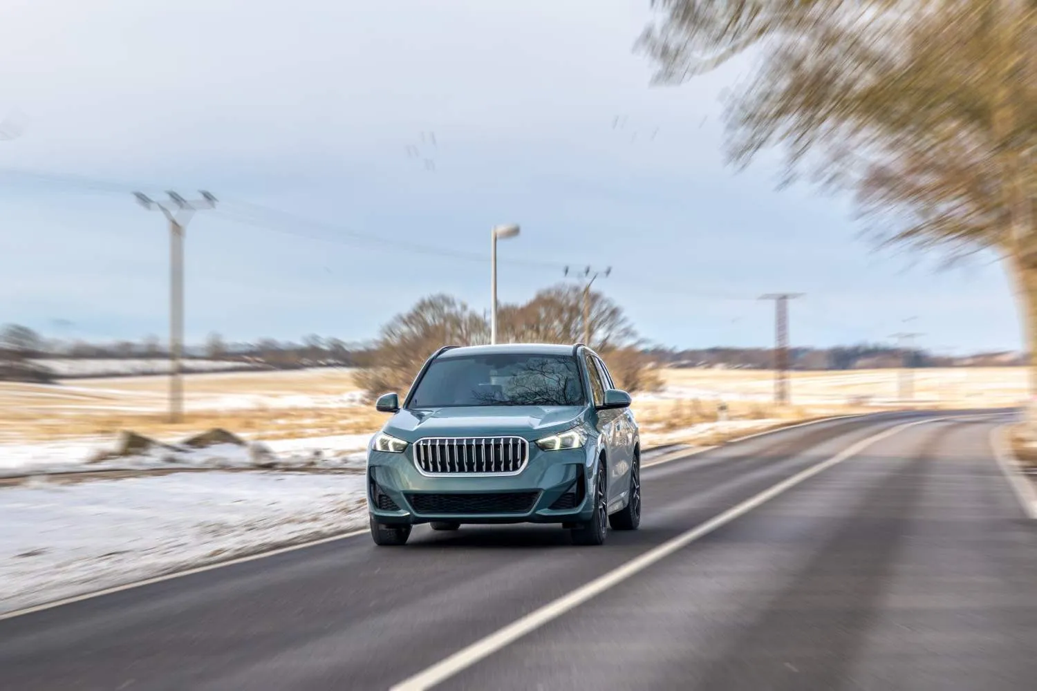 Teal SUV driving along a country road past snowy fields